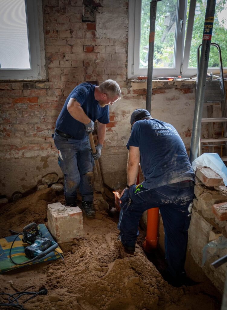 Zwei Mitarbeiter der Höft GmbH beim Freilegen und Erneuern einer Abwasserleitung im Kellerboden